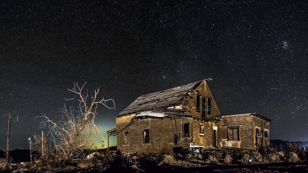 Abandoned weathered house lit against a star-filled desert night sky