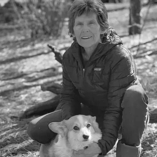Smiling woman crouching outdoors with a corgi dog