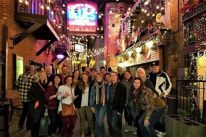 Tour group posing in a brick alley strung with lights and neon signs at night