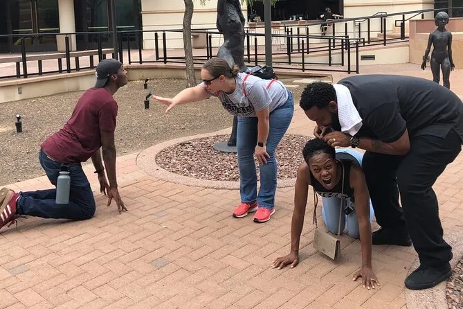 People laughing and posing playfully around statues in a downtown plaza during a scavenger hunt