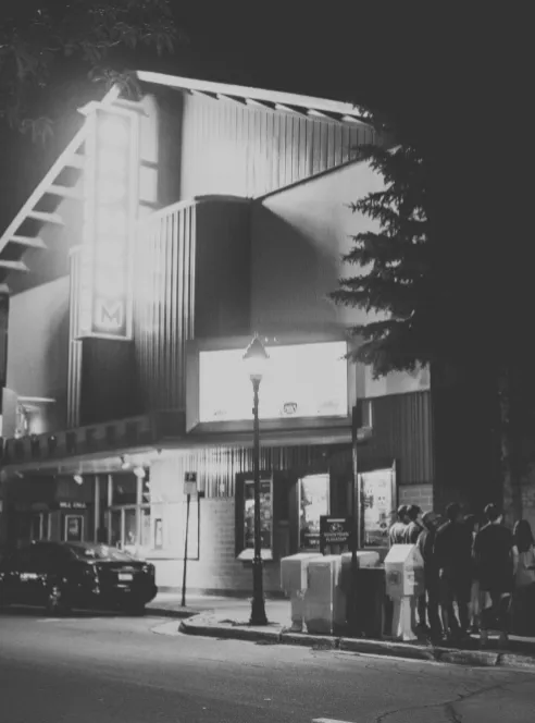 Black-and-white night shot of a theater marquee with people gathered outside