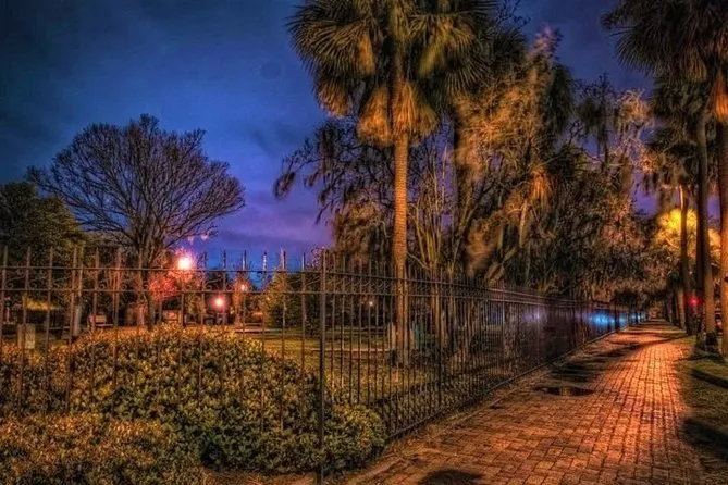 Brick pathway along an iron fence and moss-draped trees lit at dusk in Savannah