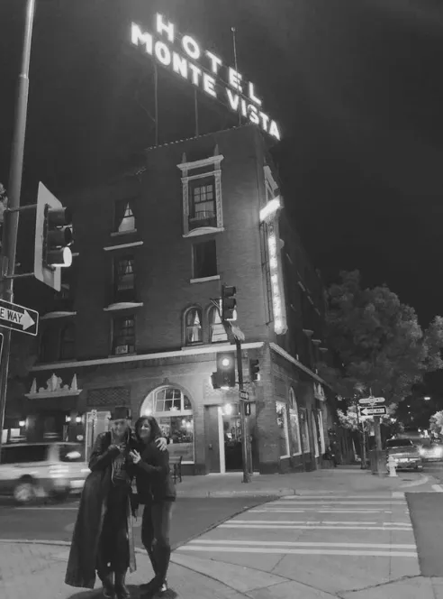 Two people posing at night beneath the lit Hotel Monte Vista sign in Flagstaff