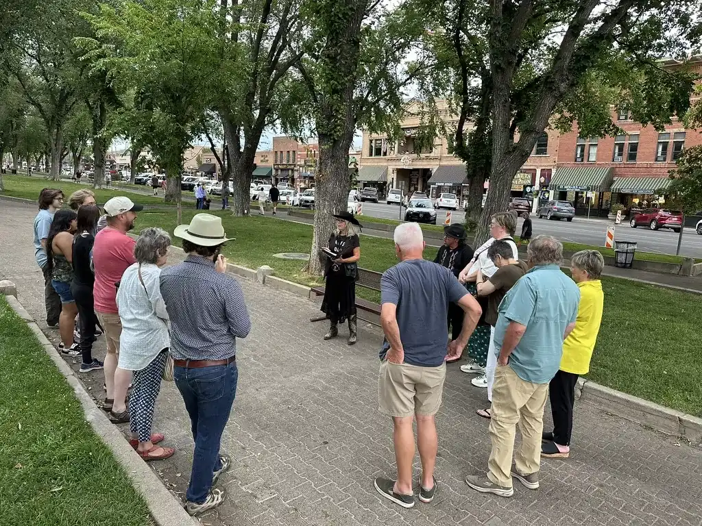 Daytime walking tour group listening to a guide in black in a tree-lined downtown plaza