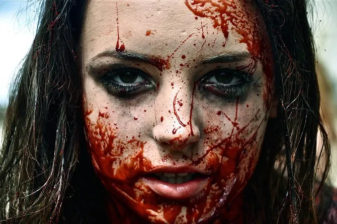 Close-up of a woman's face covered in fake blood staring at the camera