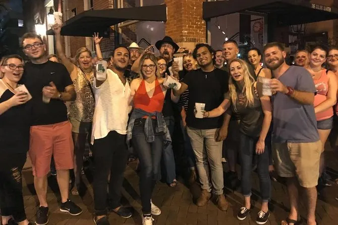 Smiling tour group posing with drinks on a brick sidewalk at night