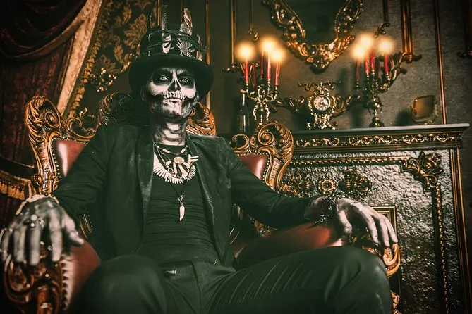 Person in skeleton face paint and feathered top hat seated in an ornate gilded chair