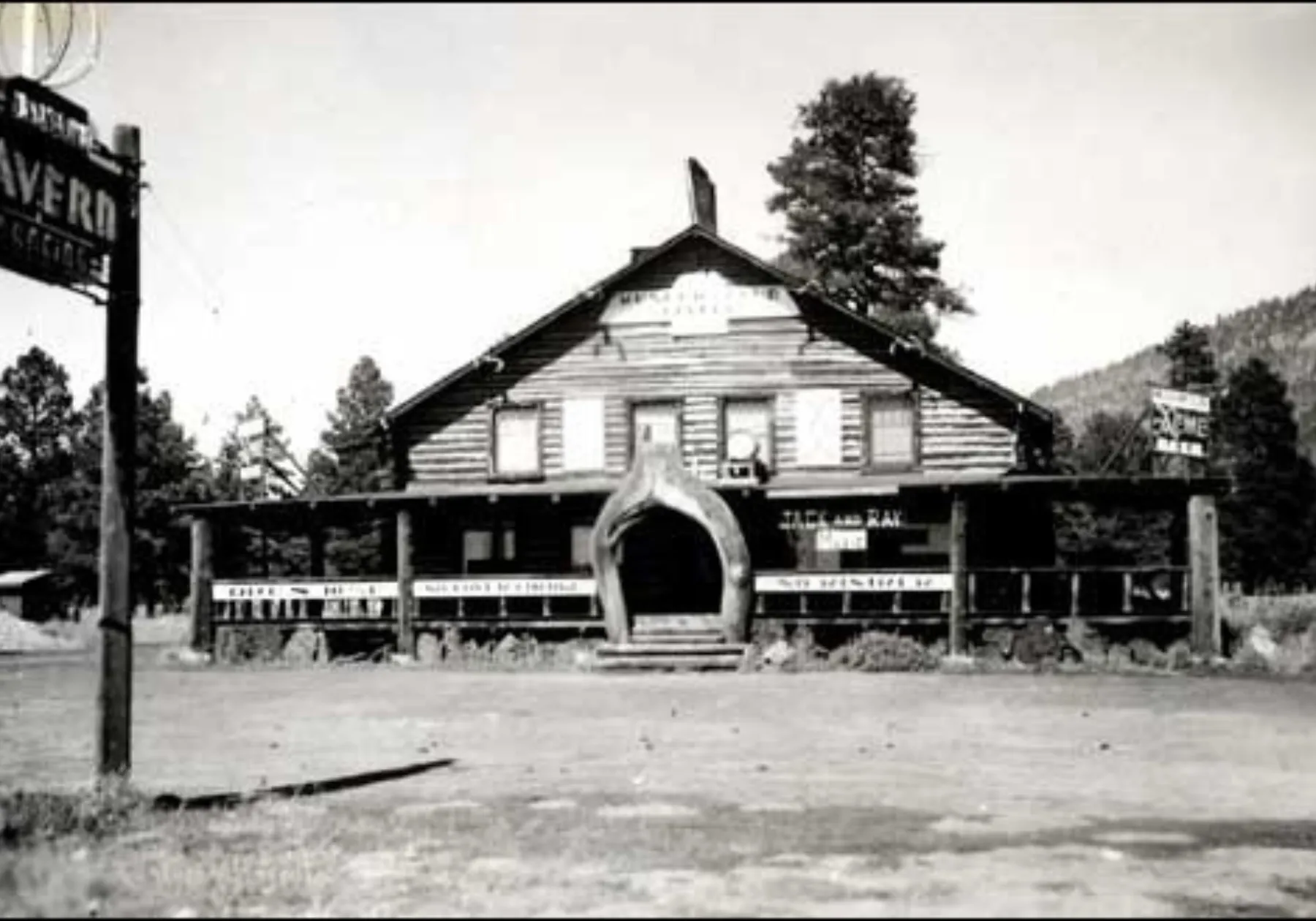 Vintage black-and-white log-cabin roadhouse tavern with a whale-jaw arched entrance