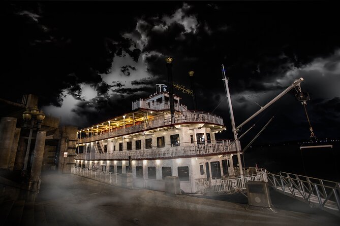 A brightly lit paddlewheel riverboat moored at night under dark clouds