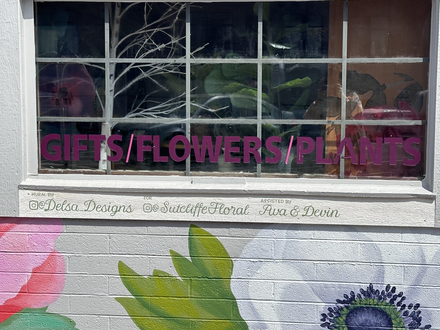 Painted anemones bloom beneath the Sutcliffe Floral shop window, with the mural credits lettered right onto the sill.