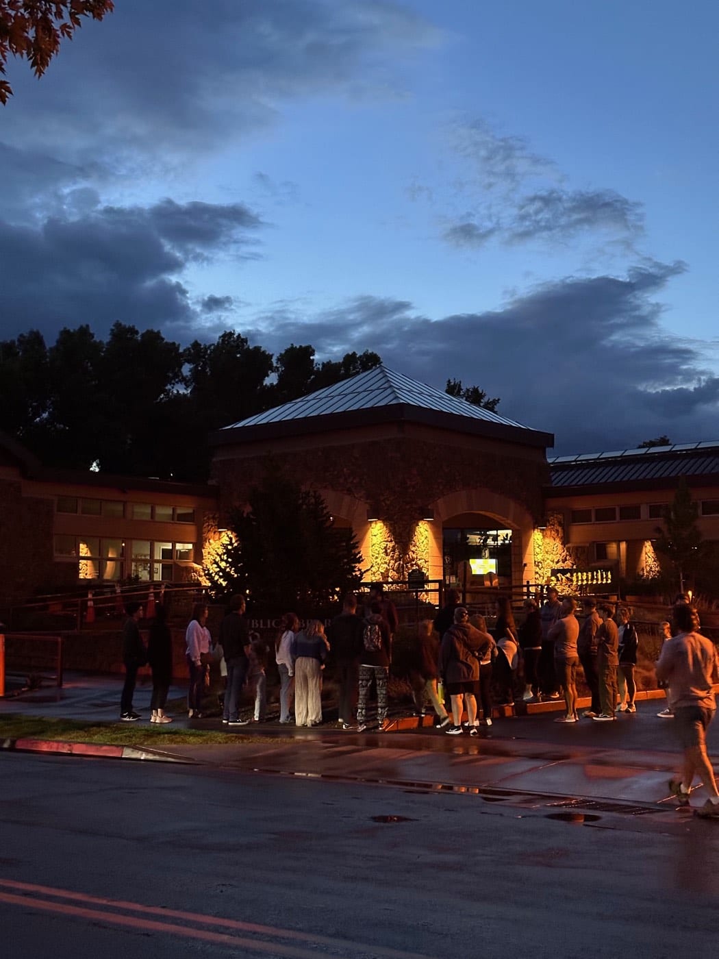 Phones come out along the walkway as the tour catches the library's glowing arches against the last blue of evening.
