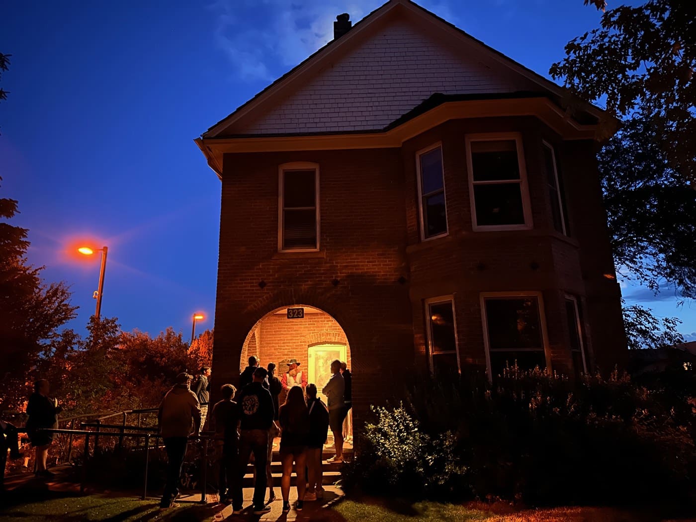 Under a deep blue night sky, the guide holds court in the Victorian's glowing doorway - the porch stop where the darker stories begin.