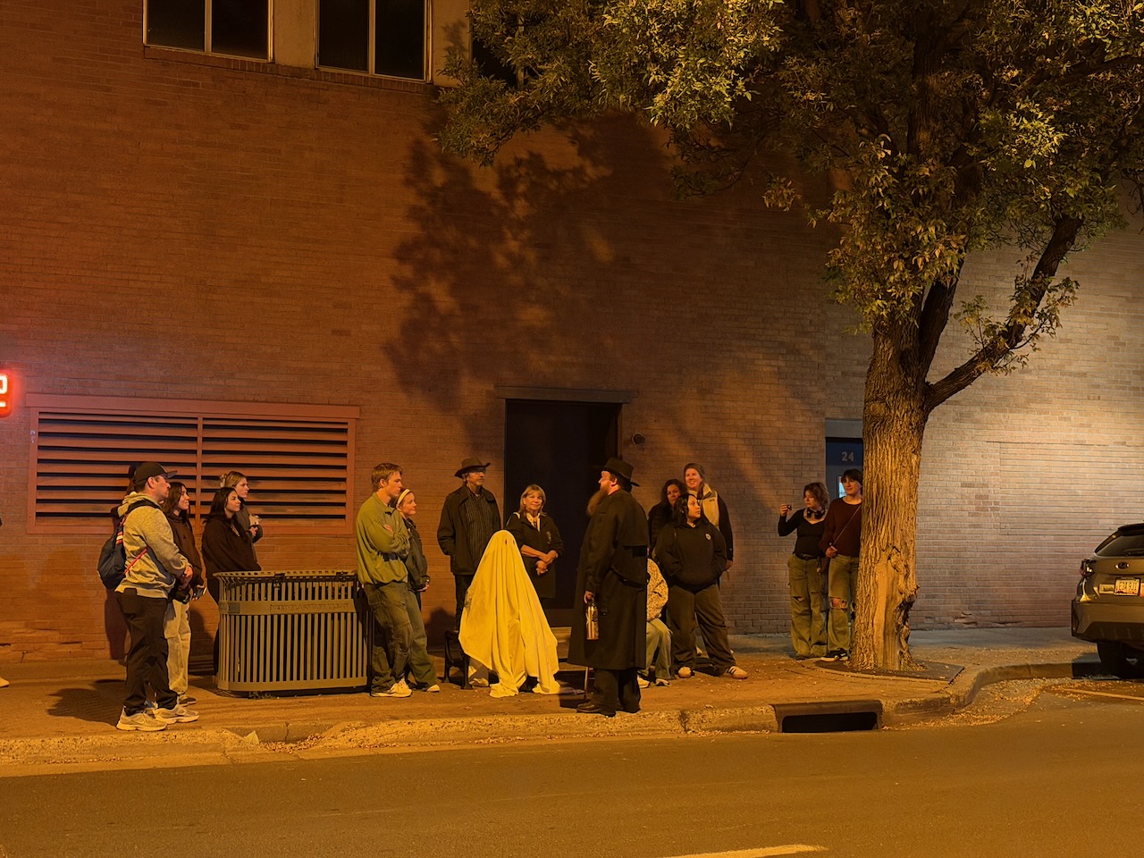 A Freaky Foot Tours group and costumed guides pose with a sheet ghost on a downtown Flagstaff sidewalk at night
