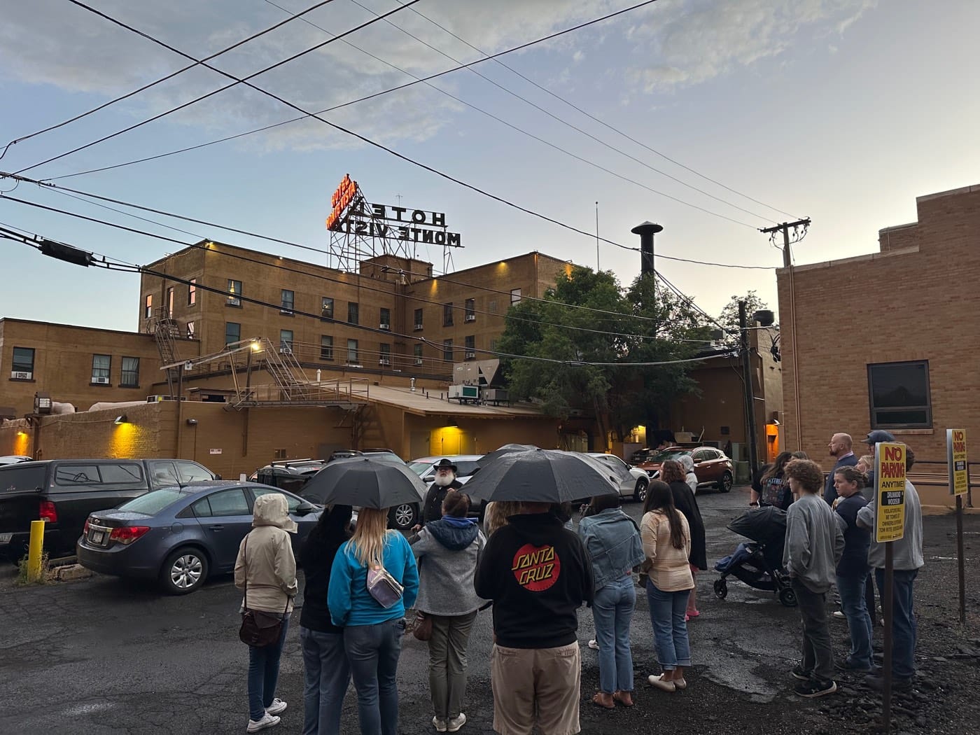 A tour group under umbrellas behind the Hotel Monte Vista, where fire escapes and service doors set the scene for the hotel’s eerier legends.