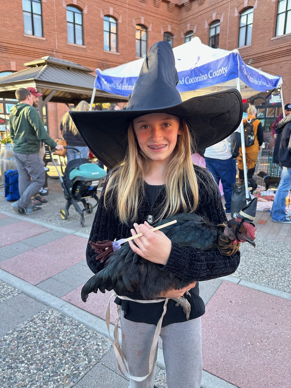 Child in a witch hat holding a chicken wearing a tiny witch hat at Howl-O-Ween 2025