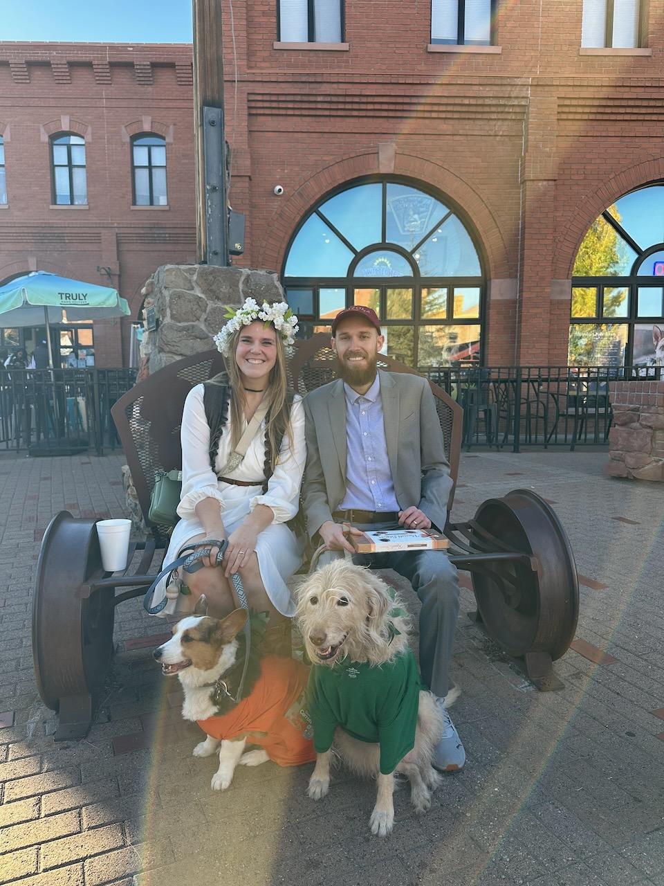 Couple on a Heritage Square bench with a corgi and a doodle in costume at Howl-O-Ween 2025