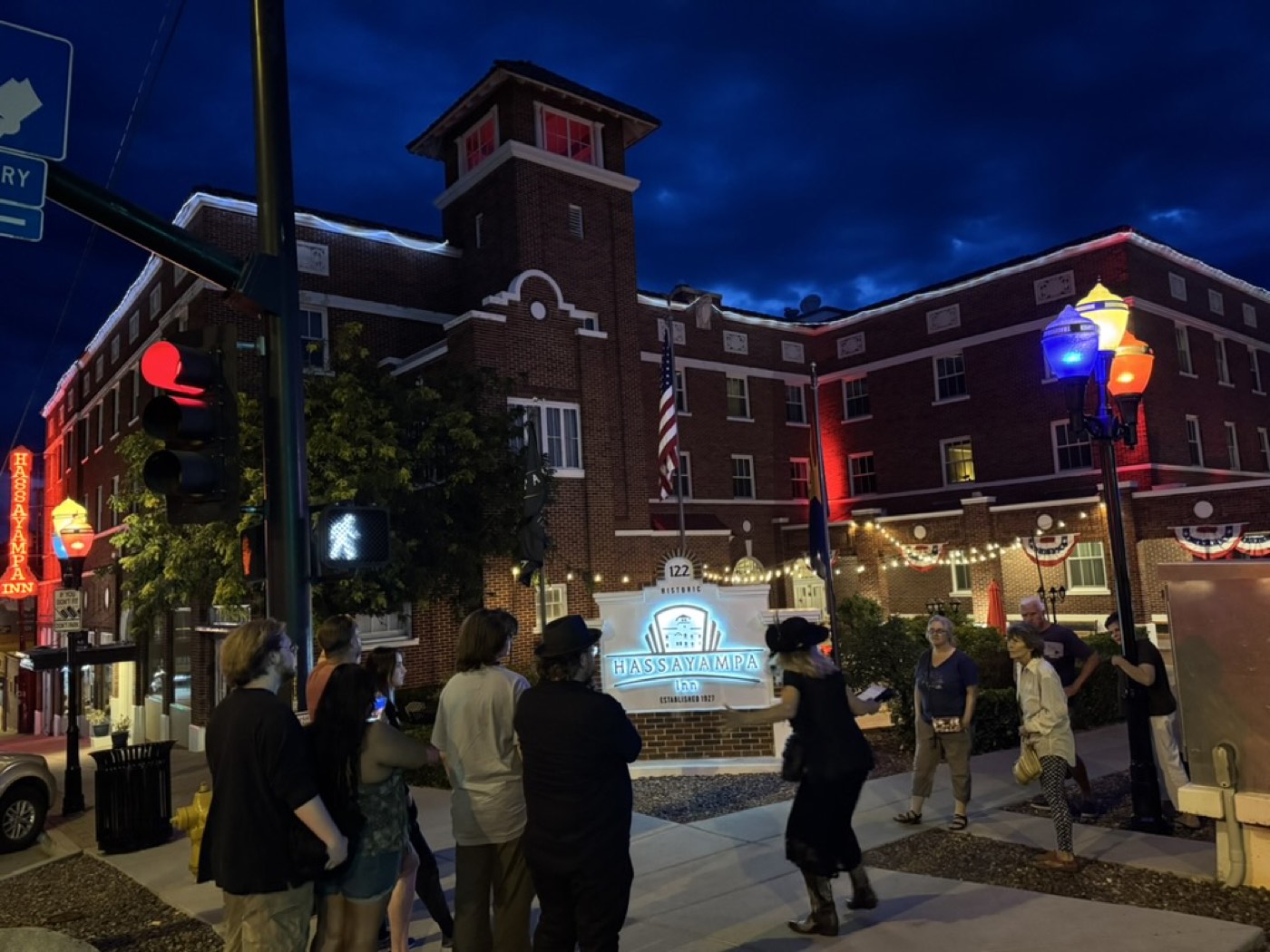 Under a brooding night sky, a costumed guide gathers guests at the glowing Hassayampa Inn sign to share why Room 426 is said to echo with weeping.