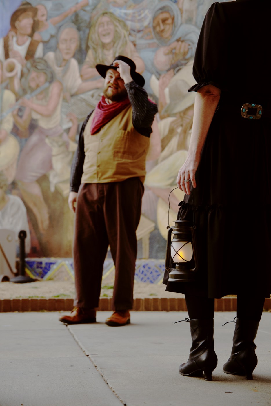 A Freaky Foot Tours guide holds a glowing lantern near the Everybody's Hometown mural in Prescott, setting the scene for tales of ghosts and unsolved crimes along Whiskey Row.