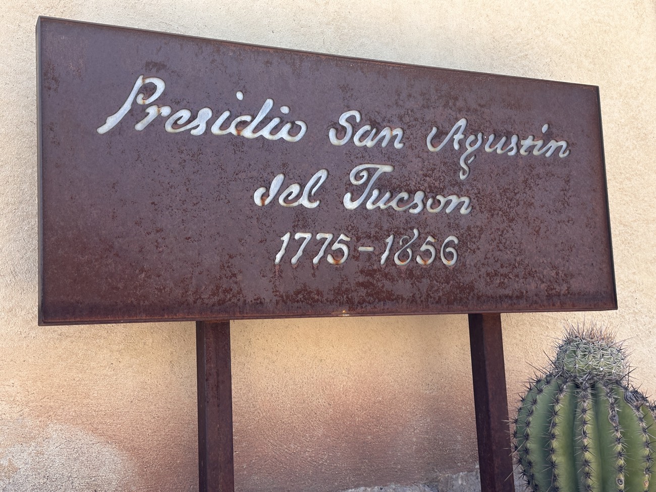 Rusted metal sign reading Presidio San Agustin del Tucson 1775 to 1856 with a saguaro cactus